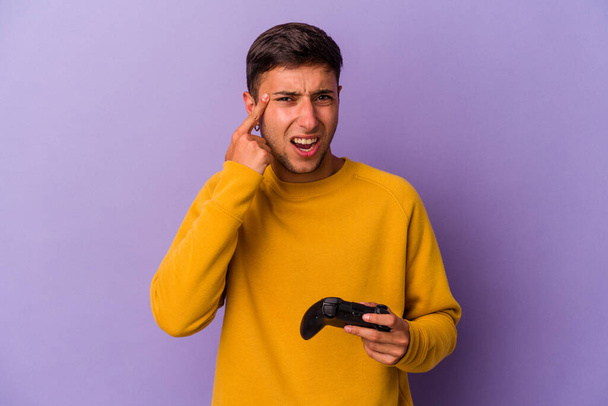 Young caucasian man holding game controller isolated on purple background  showing a disappointment gesture with forefinger. - 写真・画像