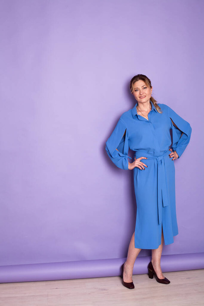 beautiful woman of 40 years in a blue dress on a purple background - Foto, Imagem
