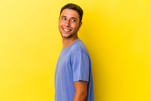 Young caucasian man with tattoos isolated on yellow background  looks aside smiling, cheerful and pleasant. - Photo, image