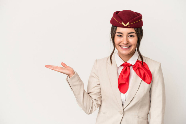 Young caucasian stewardess woman isolated on white background showing a copy space on a palm and holding another hand on waist. - Valokuva, kuva
