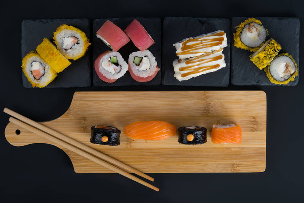 on a black table and a wooden stand, assorted Japanese rolls of tuna, salmon and baked in tempura, top view - Foto, imagen