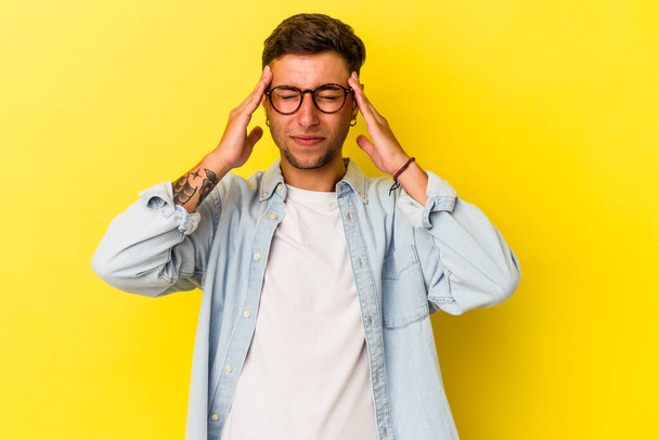 Young caucasian man with tattoos isolated on yellow background  having a head ache, touching front of the face. - Photo, image