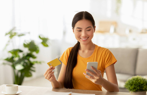 Łatwa płatność zbliżeniowa. Szczęśliwy koreański lady dokonywania zakupów przez internet, za pomocą smartfona i posiadania karty kredytowej - Zdjęcie, obraz