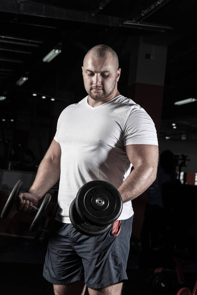 Male bodybuilder engaged with dumbbells in the gym - Foto, afbeelding