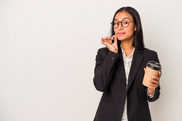 Jonge zakenvrouw latin holding een take away koffie geïsoleerd op witte achtergrond met vingers op de lippen houden van een geheim. - Foto, afbeelding