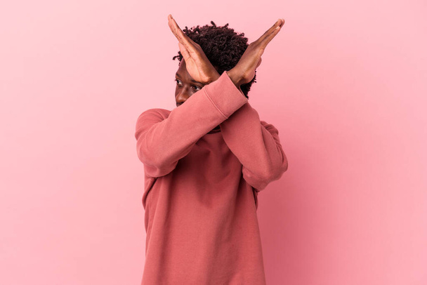Jonge Afro-Amerikaanse man geïsoleerd op roze achtergrond houden van twee armen gekruist, ontkenning concept. - Foto, afbeelding