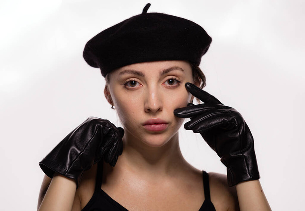 Portret wspaniałej młodej modelki w czarnym berecie i skórzanych rękawiczkach pozujących na białym tle. Zbliżenie twarz młodej pięknej kobiety ze zdrową, czystą skórą - Zdjęcie, obraz