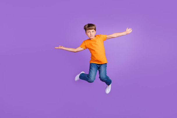 Full length body size photo boy jumping up orange t-shirt jeans isolated pastel violet color background - Фото, изображение