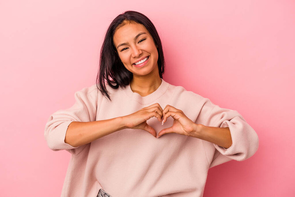 fiatal latin nő elszigetelt rózsaszín háttér mosolygó és mutató szív alakú kezek. - Fotó, kép