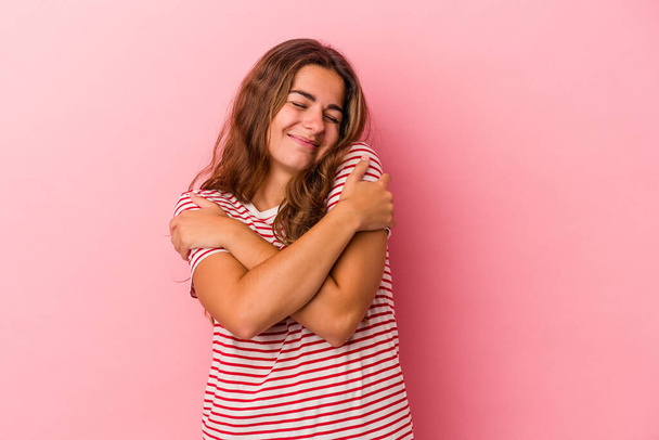Joven mujer caucásica aislada sobre los abrazos de fondo rosa, sonriente despreocupada y feliz. - Foto, imagen