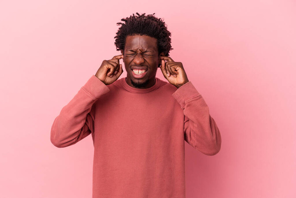 Jovem afro-americano isolado no fundo rosa cobrindo orelhas com as mãos. - Foto, Imagem