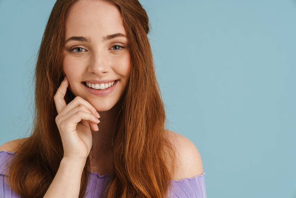 Young ginger woman smiling and looking at camera isolated over blue background - Foto, afbeelding