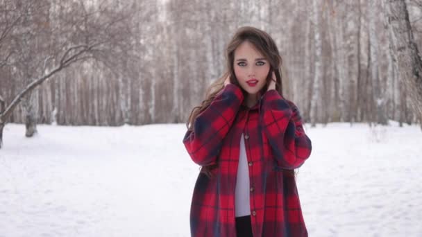 Fiatal nő hullámos haj áll és megható arc a téli erdőben - Felvétel, videó
