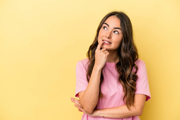 Young caucasian woman isolated on yellow background looking sideways with doubtful and skeptical expression. - Photo, Image