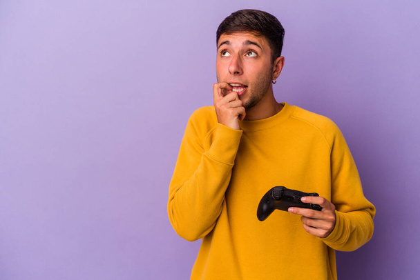 Jonge blanke man houden spel controller geïsoleerd op paarse achtergrond ontspannen denken over iets op zoek naar een kopieerruimte. - Foto, afbeelding