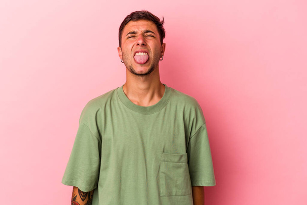 Young caucasian man with tattoos isolated on yellow background  funny and friendly sticking out tongue. - Фото, изображение