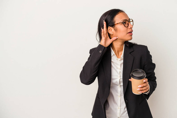 Νεαρή επιχειρηματίας Λατίνα γυναίκα κρατώντας ένα take away καφέ απομονωμένη σε λευκό φόντο προσπαθεί να ακούσει ένα κουτσομπολιό. - Φωτογραφία, εικόνα