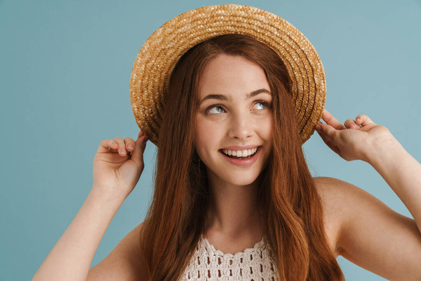 Young ginger woman in straw hat smiling and looking aside isolated over blue background - Foto, Imagen