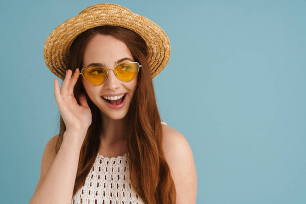 Young ginger woman in sunglasses smiling and looking aside isolated over blue background - Foto, immagini