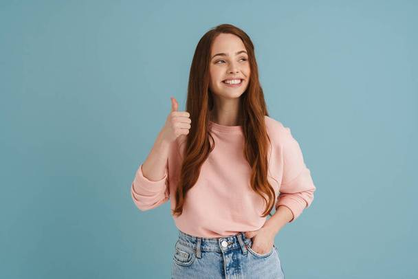 Young ginger woman smiling and showing thumb up at camera isolated over blue background - Foto, Bild