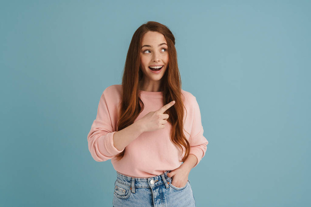 Young ginger woman smiling and pointing finger aside isolated over blue background - Fotoğraf, Görsel