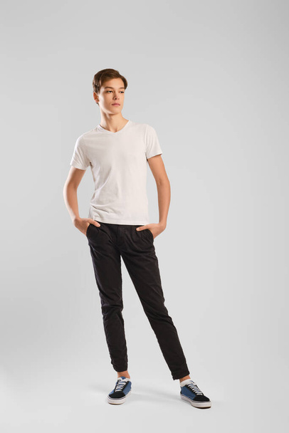Nice man in white t-shirt, black trousers and sneakers posing over grey background. Studio model tests. - Valokuva, kuva
