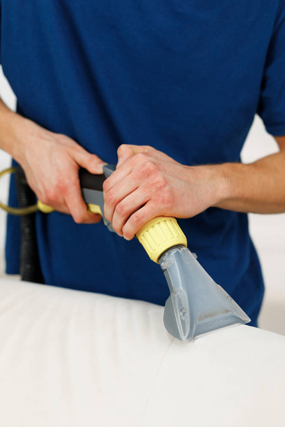 Zamknij zdjęcie pracownika firmy sprzątającej odkurzającego poduszkę na białej sofie - Zdjęcie, obraz