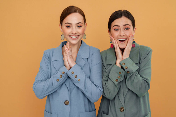 Young two women wearing jackets smiling and looking at camera isolated over yellow background - Foto, Imagem