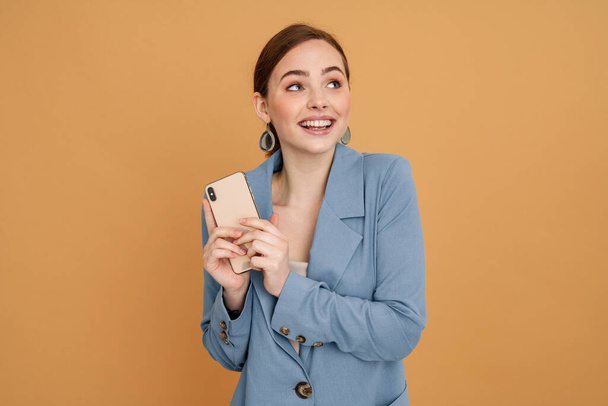 Young ginger woman smiling while using mobile phone isolated over yellow background - Photo, image