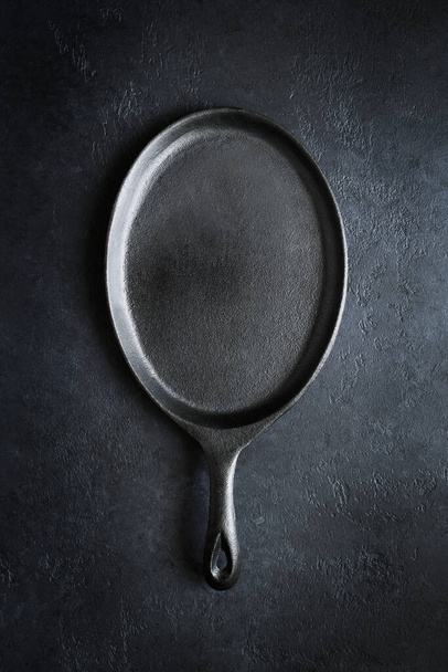 Empty oval cast iron frying pan on dark slate backgound, top view - Фото, зображення
