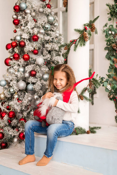 Mädchen umarmt Zwergspielzeug auf dem Hintergrund eines Weihnachtsbaums - Foto, Bild