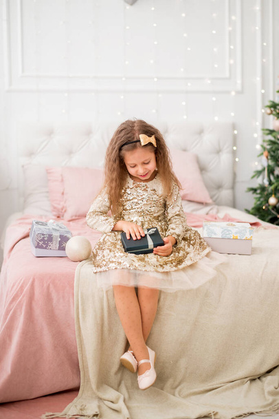 Tyttö kultaisessa mekossa avaa joululahjan. Uuden vuoden valokuva - Valokuva, kuva