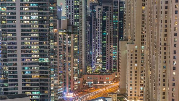 Overview to JBR and Dubai Marina skyline with modern high rise skyscrapers waterfront living apartments aerial timelapse during all night with lights turning off. Traffic on road intersection and footbridge - Fotó, kép