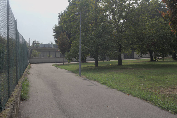 carril bici bordeado por una rejilla de metal junto a un parque en un día nublado - Foto, imagen