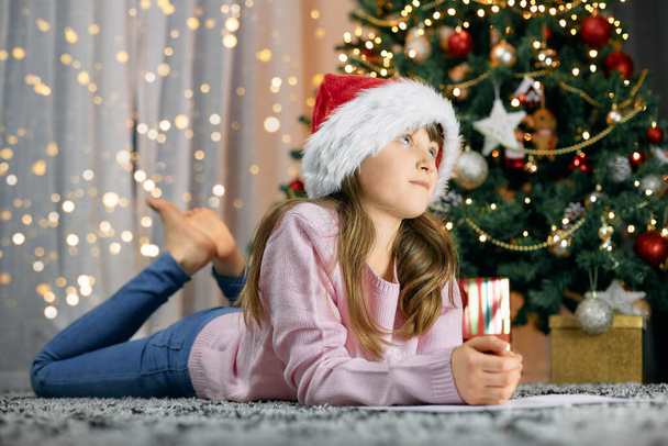Ein süßes Mädchen liegt am Weihnachtsbaum und träumt. Träume werden wahr. Kinder warten auf Neujahr und Weihnachten - Foto, Bild