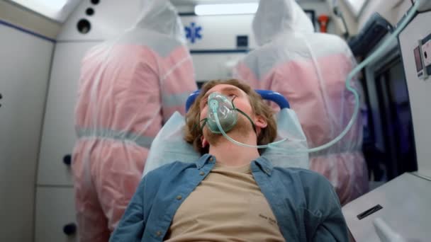 Man zit op brancards in een noodvoertuig. Slachtoffer ademt zuurstofmasker in - Video