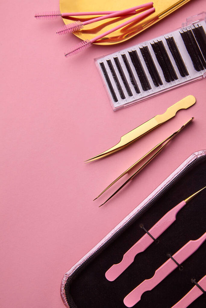 Golden Tools for Eyelash Extension Procedure. Golden tweezers,palete with Eyelash, brushes for eyelash on golden plate. Pink background.Beauty and fashion concept - Foto, afbeelding