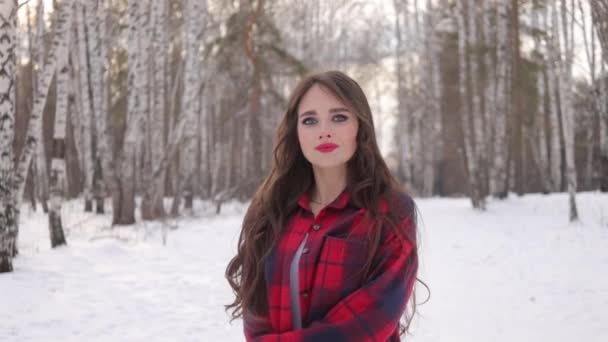 Urocza kobieta z długimi włosami spacerująca po zaśnieżonym lesie - Materiał filmowy, wideo