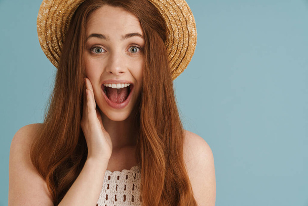 Young ginger woman in straw hat expressing surprise on camera isolated over blue background - Fotografie, Obrázek
