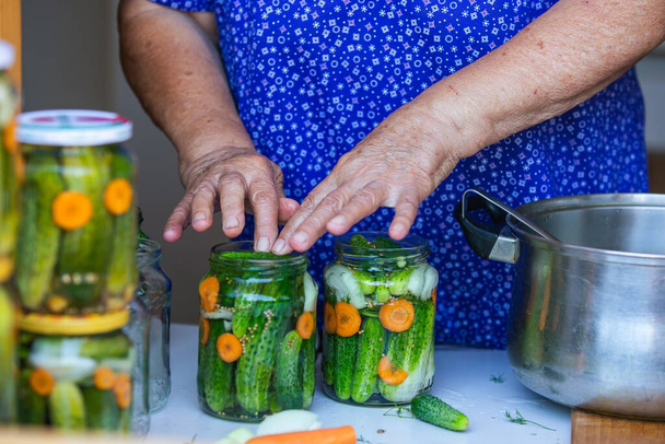 Process of canning a cucumber, senior woman canning fresh cucumbers with onion and carrots, homemade product, food concept - Fotó, kép
