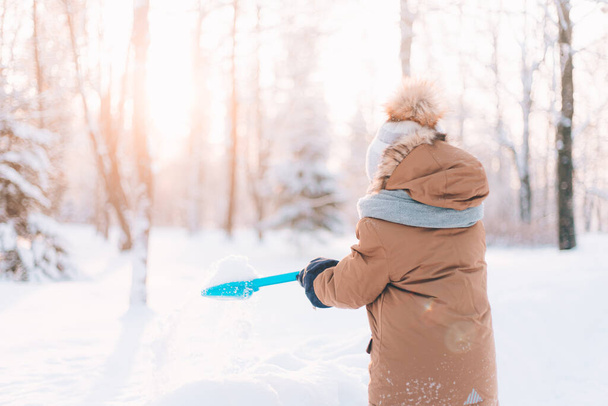 少年はシャベルライフスタイルで雪を投げます。冬の散歩。子供の冬のレジャーに関する記事。芸能 - 写真・画像
