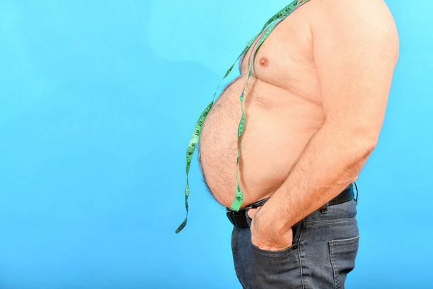 Um homem gordo e gordo com uma barriga grande segura um centímetro ao redor do pescoço para medir sua cintura. - Foto, Imagem