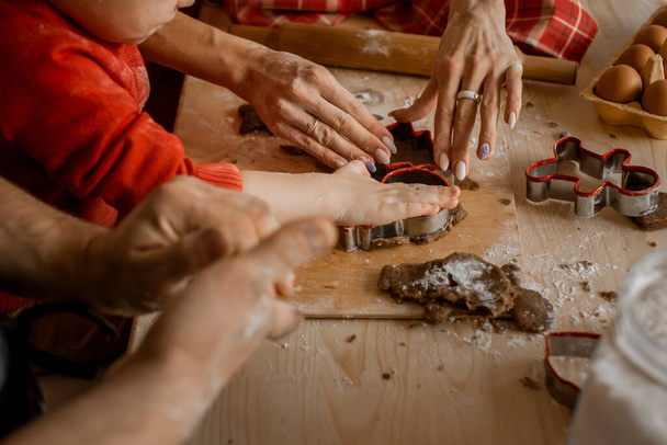 Vue rapprochée latérale des mains d'un membre de la famille découpant différentes formes de Noël à partir de pâte crue pour cuire des biscuits au pain d'épice de Noël festifs - Photo, image