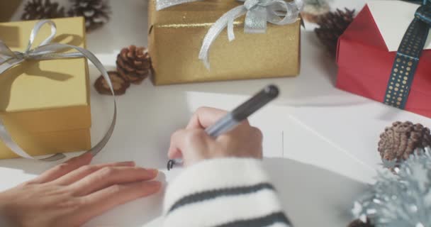 Κοντινό πλάνο των χεριών κορίτσι γραπτώς ευχετήρια κάρτα χειμώνα χριστουγεννιάτικα στολίδια στο τραπέζι. Ελάχιστη δημιουργική επίπεδη lay των Χριστουγέννων παραδοσιακή σύνθεση και την εποχή των διακοπών του νέου έτους. - Πλάνα, βίντεο