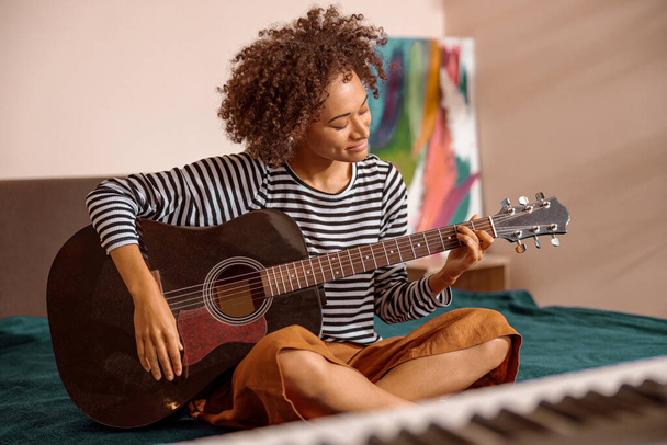 Mujer joven multirracial tocando la guitarra en casa - Foto, imagen