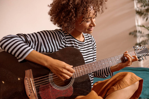 Mosolygó fiatal nő gitározik otthon - Fotó, kép