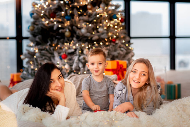 Happy cheerful family near Christmas tree. Mother and kids wearing pajama having fun near tree in the morning. Merry Christmas and Happy Holidays concept - Foto, Imagem