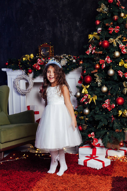 kleines lockiges Mädchen am Weihnachtsbaum mit Geschenken Silvesterlichtergirlanden - Foto, Bild