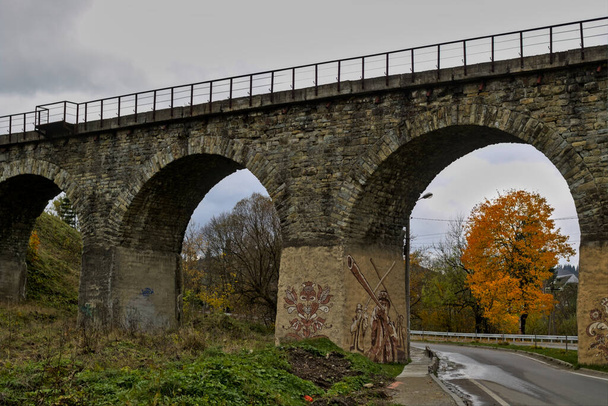 Alte österreichische Brücke Viadukt in Worochta Dorf der Karpaten Ukraine. Herbstliche Berglandschaft - vergilbte und gerötete Herbstbäume kombiniert mit grünen Nadeln. - Foto, Bild