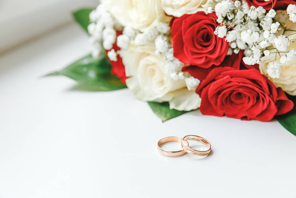白い背景に横たわる白い赤い色の金の結婚指輪と花の花束。愛の宣言春。結婚式のカードバレンタインデーの挨拶。結婚指輪だ。結婚式の詳細. - 写真・画像